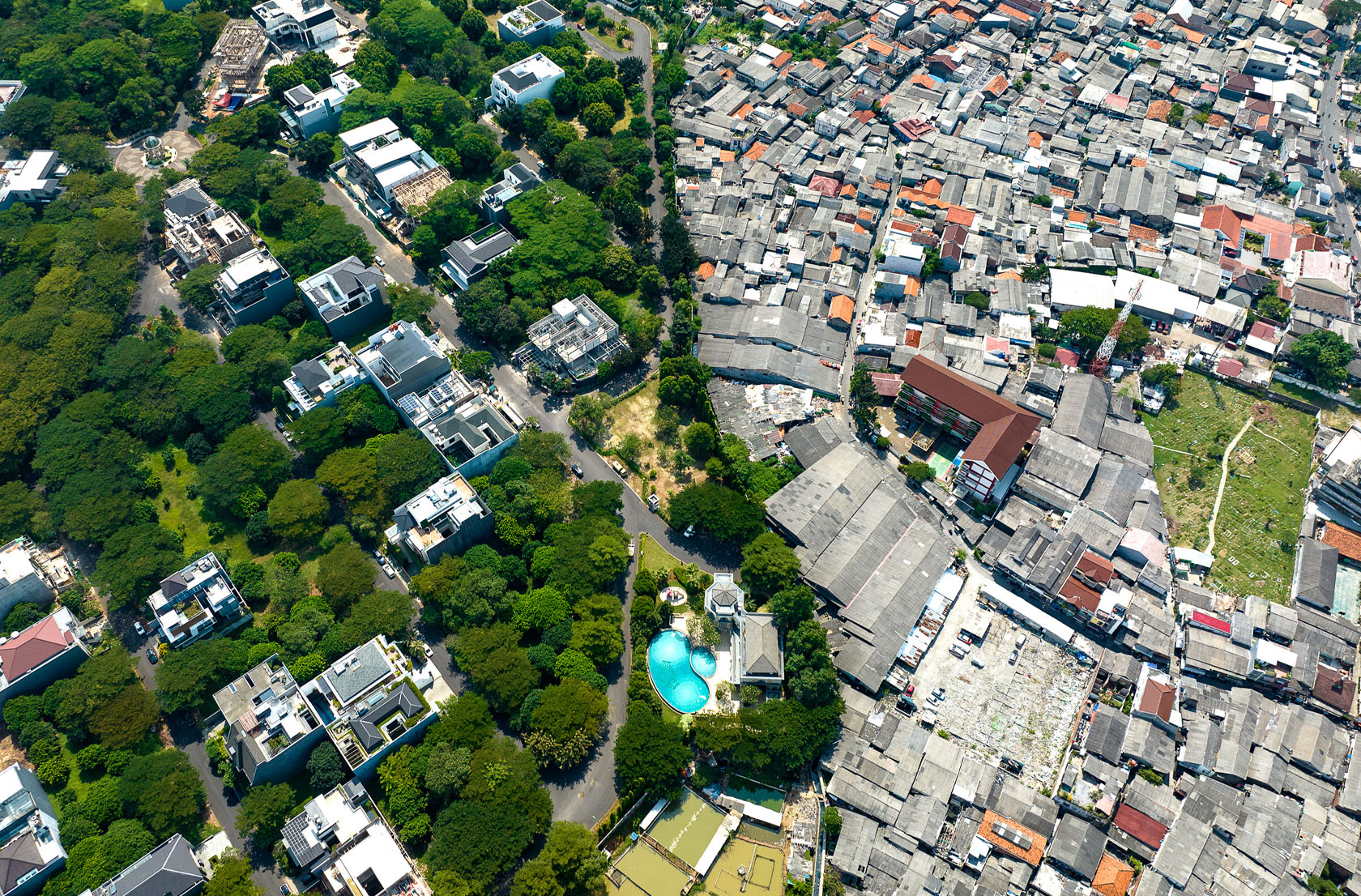 Pictured are large, luxurious homes (left) and smaller, densely packed dwellings (right), highlighting extreme wealth inequality in northern Jakarta, Indonesia. Image credit: Johnny Miller (photographer).